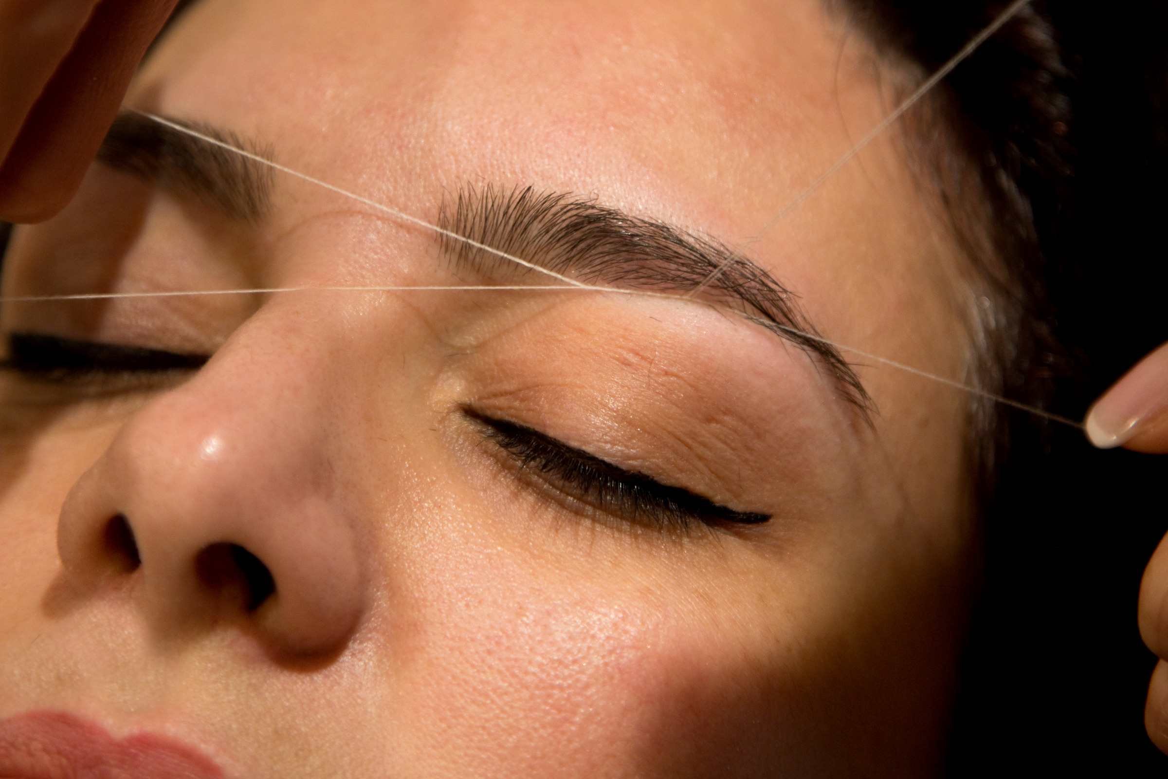 Close-up eyebrow threading in progress